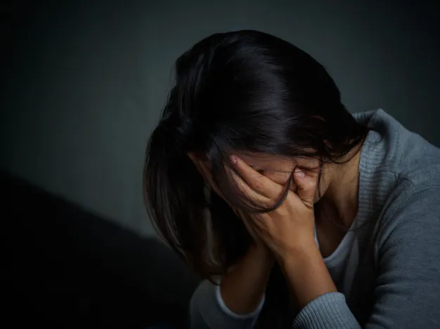 Mulher triste abraçando os joelhos em quarto vazio — sentimento de distância espiritual